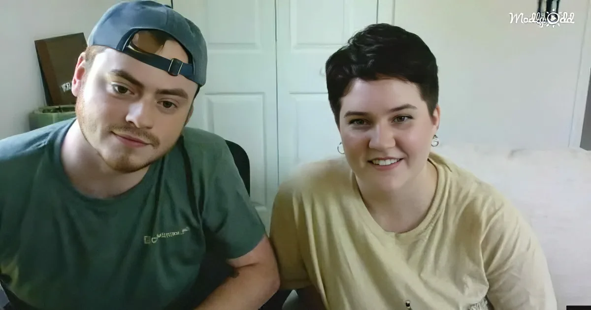 Two individuals are seated indoors, one wearing a green shirt and cap, the other in a beige shirt, both smiling.