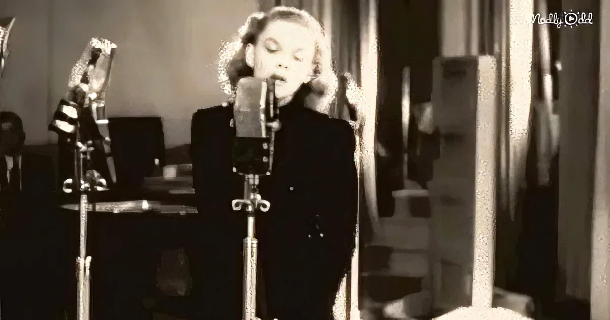 A woman in a dark coat sings into a microphone in a recording studio.