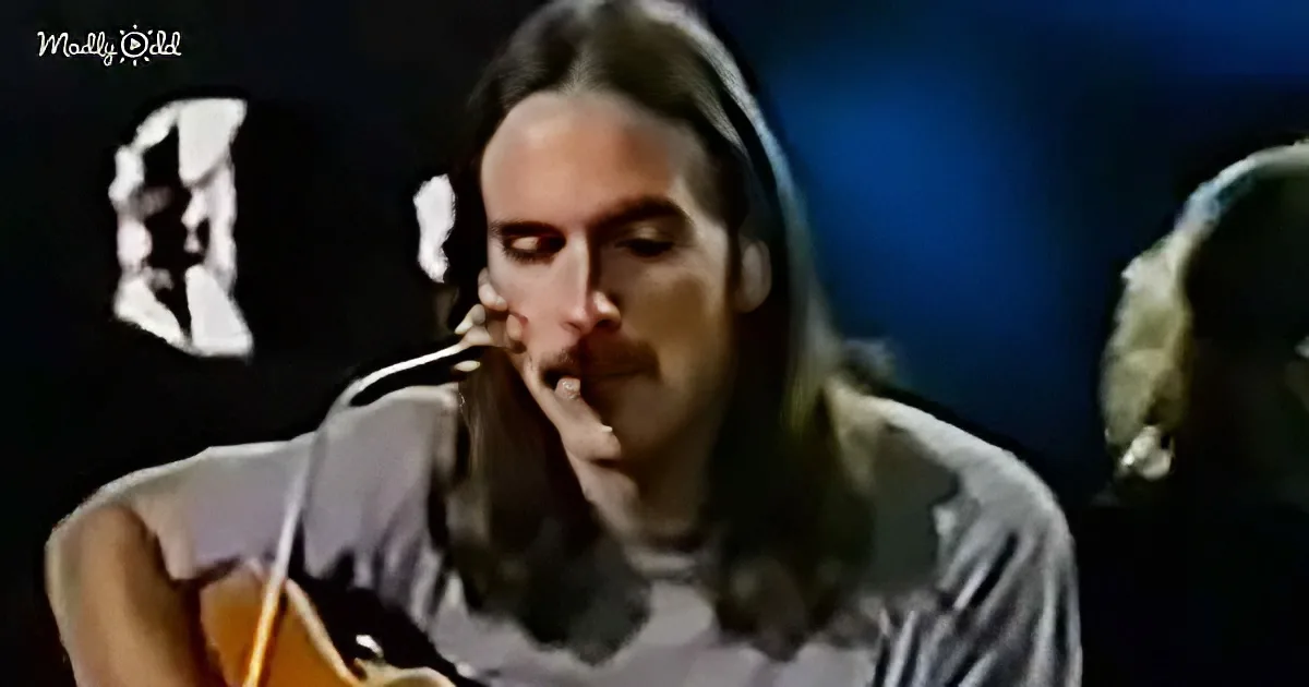 A man with long hair and a beard sings into a microphone, wearing a striped shirt.