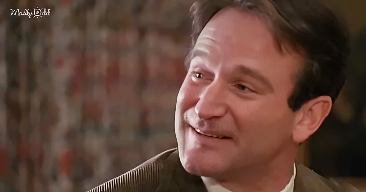A man with short brown hair and a slight smile, wearing a brown jacket, is looking to the side.