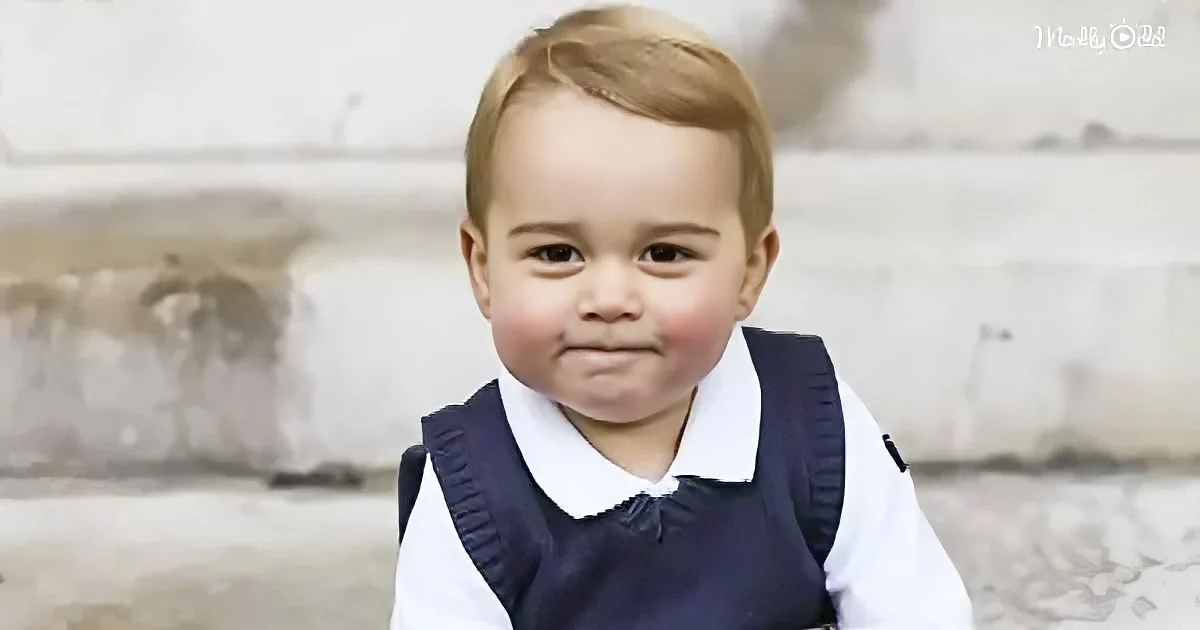 A young boy with blonde hair, wearing a navy vest and white shirt, stands outdoors with a neutral expression.