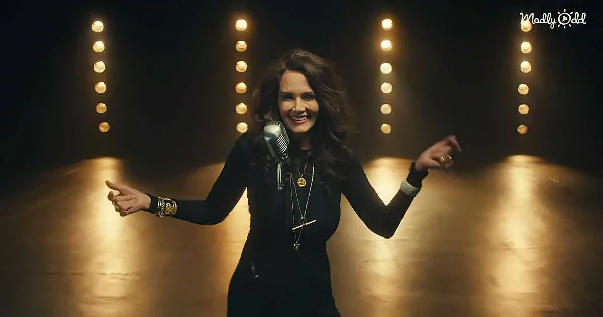A woman in a black outfit stands on stage with a microphone, surrounded by illuminated columns.