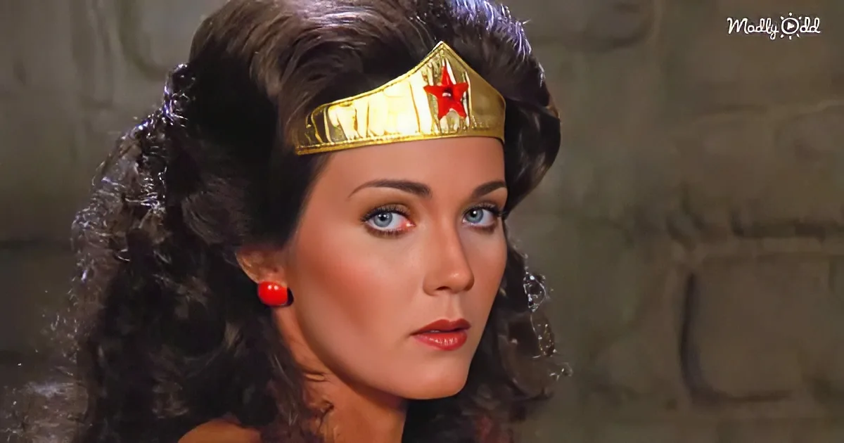 A woman with dark hair, wearing a gold Wonder Woman tiara and red earrings, stands against a textured background.