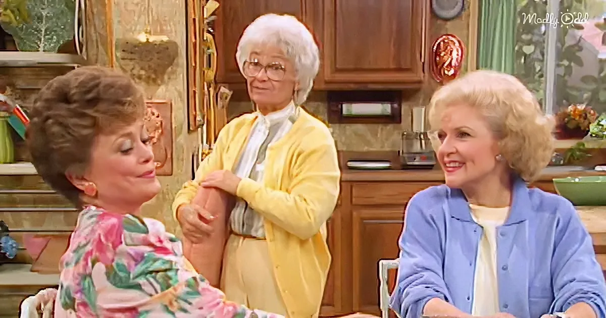 Three women in a kitchen, one in yellow adjusting another's sleeve, while the third smiles.