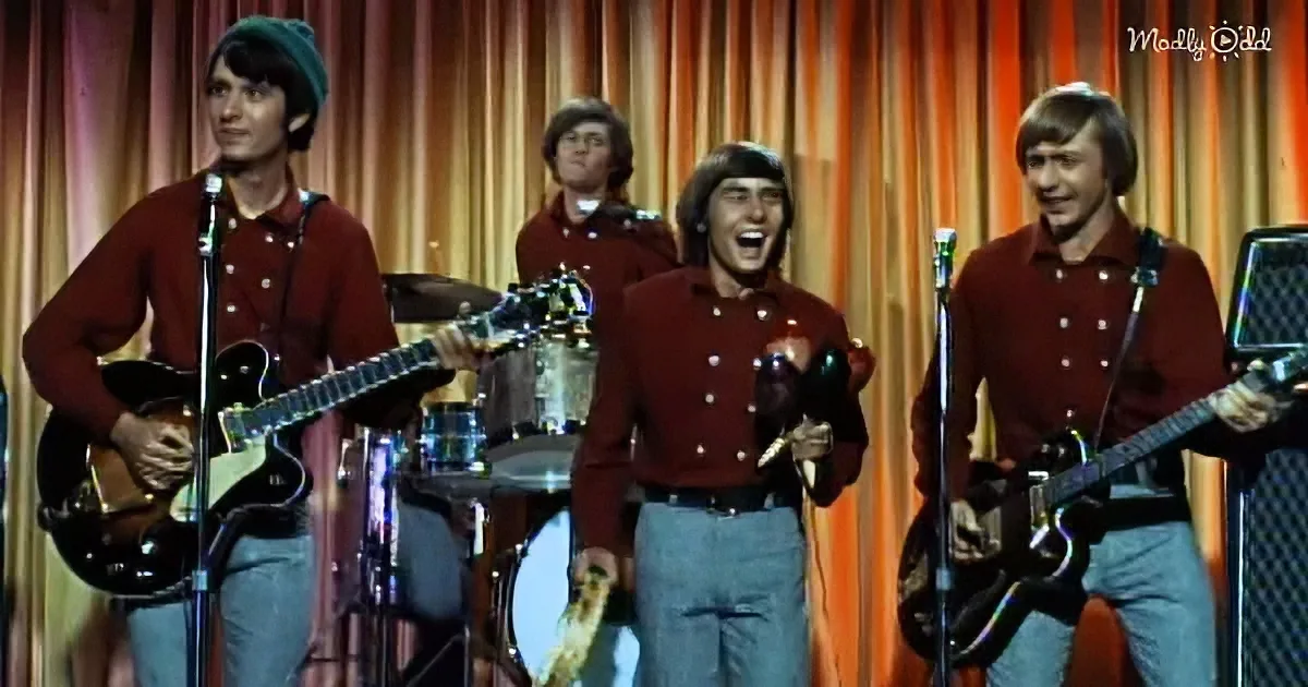 A group of musicians in red shirts and jeans performs on stage with microphones and instruments.