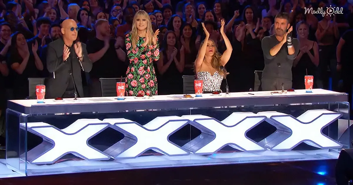 Judges on stage with raised hands, audience clapping, large "XXXX" sign in foreground.