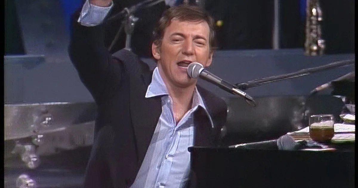 A man in a suit and tie, looking to the side, with a blurred background.