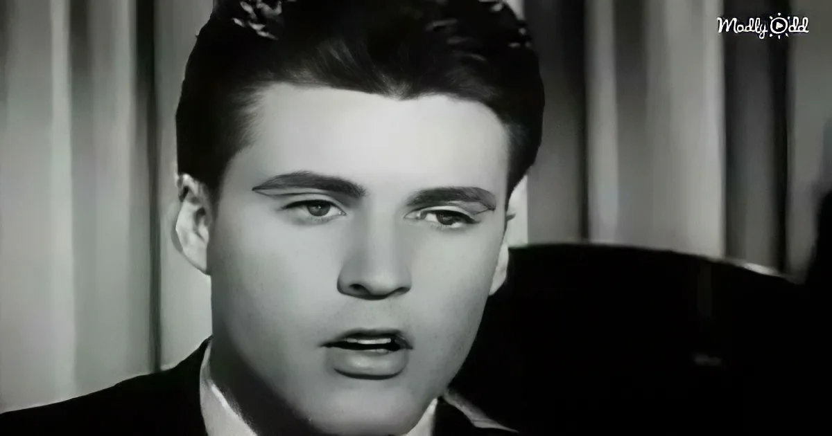A man in a suit sings passionately, his mouth open, against a blurred curtain backdrop.