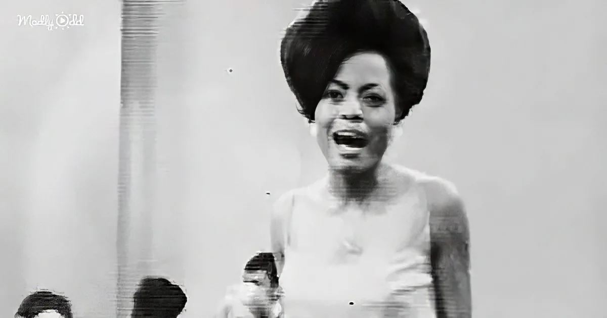 A woman in a white dress with a large, voluminous hairstyle is singing on stage.