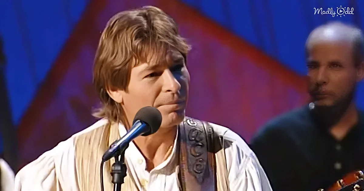 A man with long hair and a white shirt sings into a microphone, wearing a guitar strap.