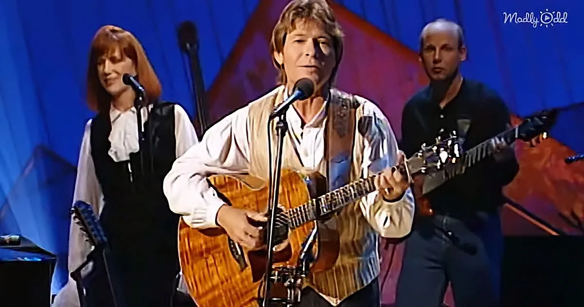 A man plays guitar on stage, singing into a microphone, with two other musicians behind him.
