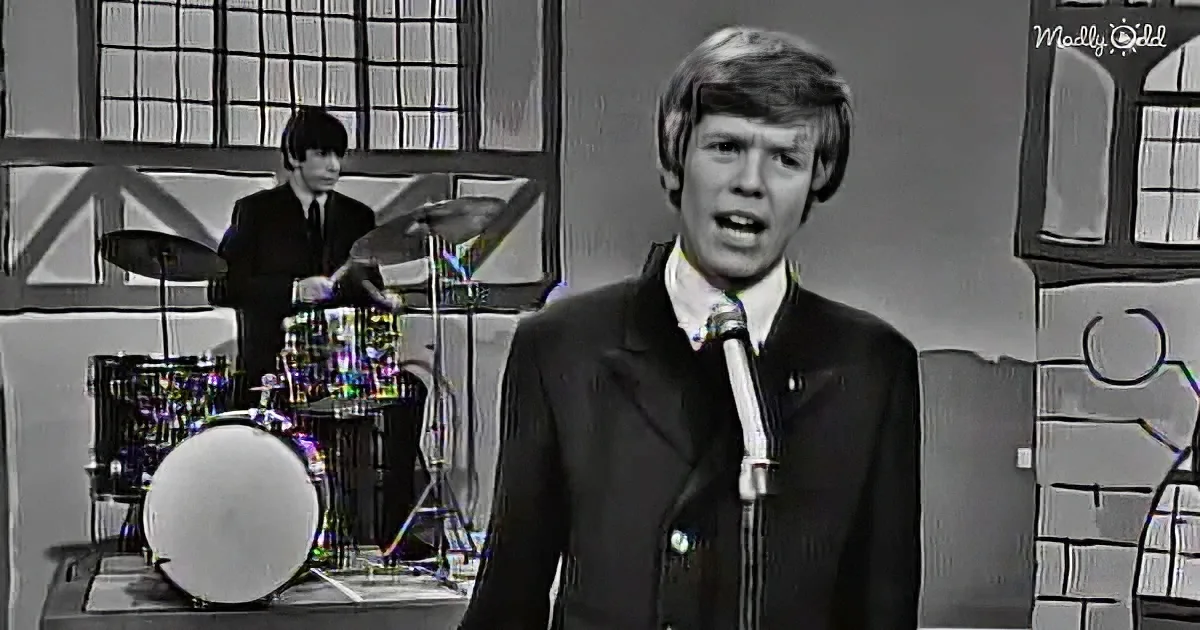 A man in a suit sings into a microphone, with a drummer in the background and a stylized backdrop.