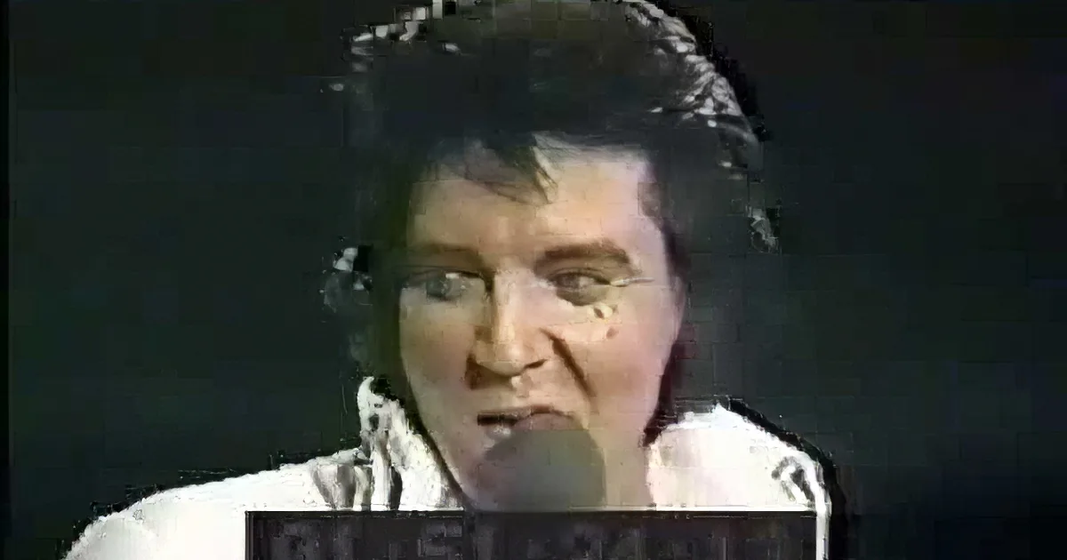 Elvis Presley in a white suit singing into a microphone, with a dark background.