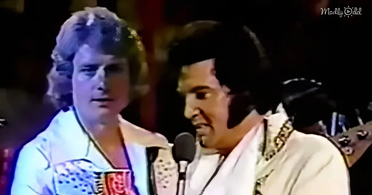Elvis Presley in white suit singing into microphone, another man in background.