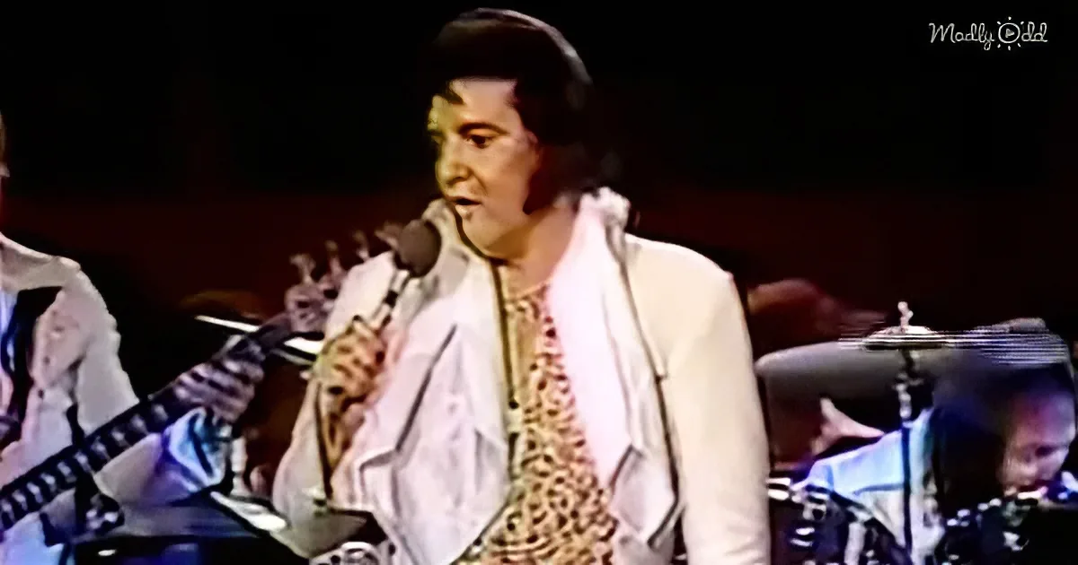 A person in a white jacket and leopard print scarf sings into a microphone on stage.