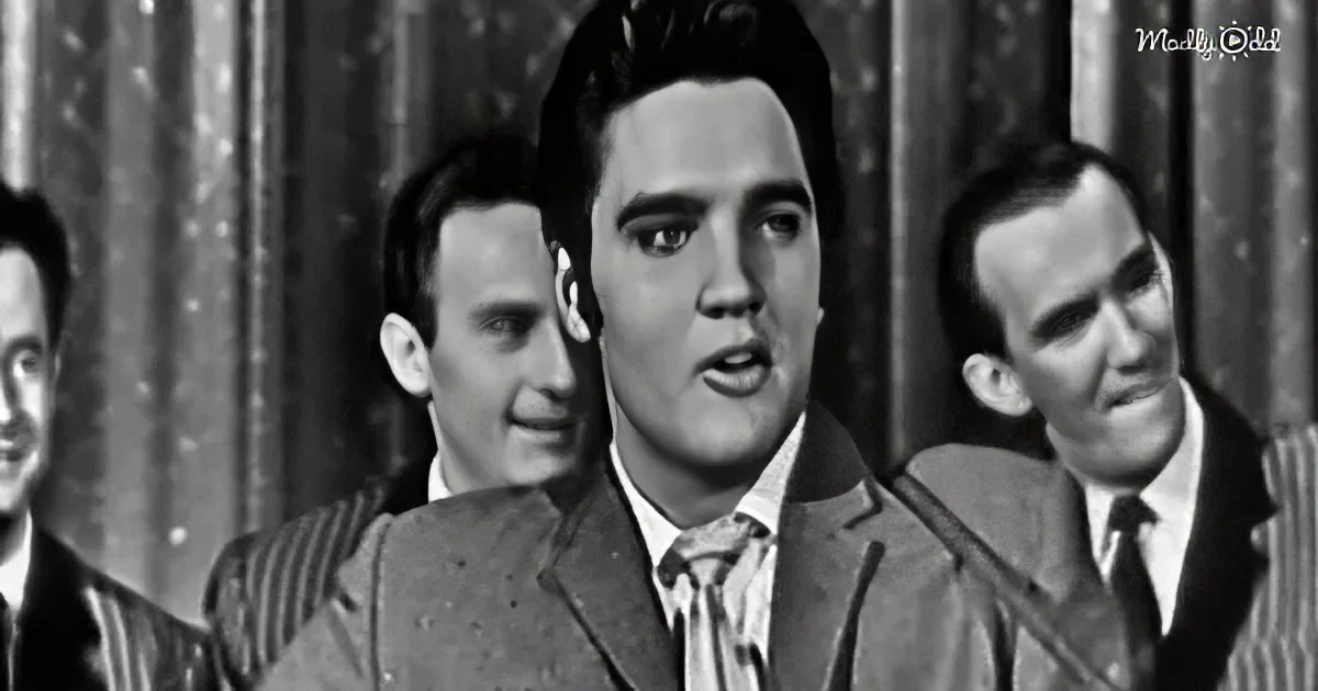 Elvis Presley in a suit and tie, singing with a band behind him.