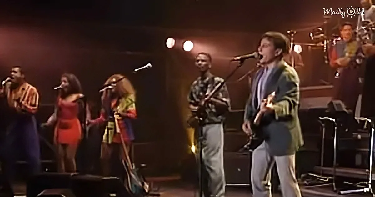 A man in a suit sings passionately on stage with a band and backup singers.
