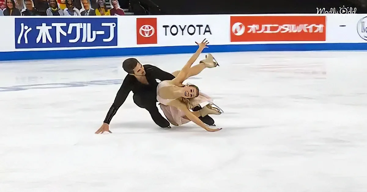 A figure skating couple performs a dramatic fall on the ice, showcasing their skills and artistry.