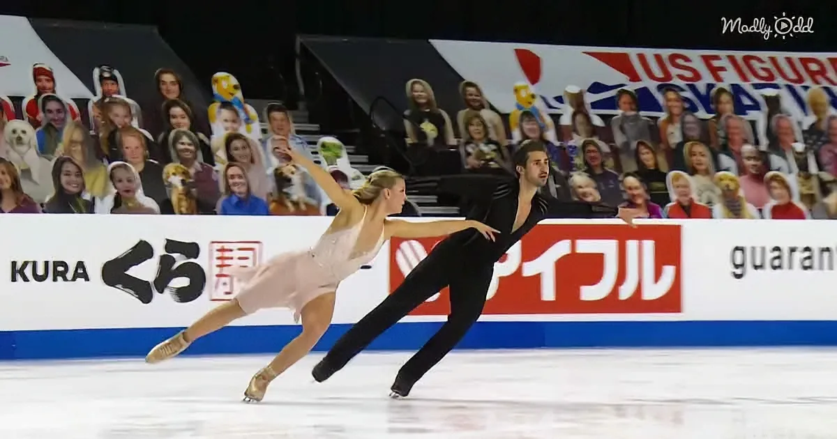 A figure skating pair glides gracefully on ice, surrounded by a cheering crowd and advertisements.