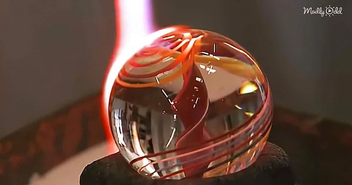 A glass sculpture with swirling red and orange patterns is being heated by a torch.
