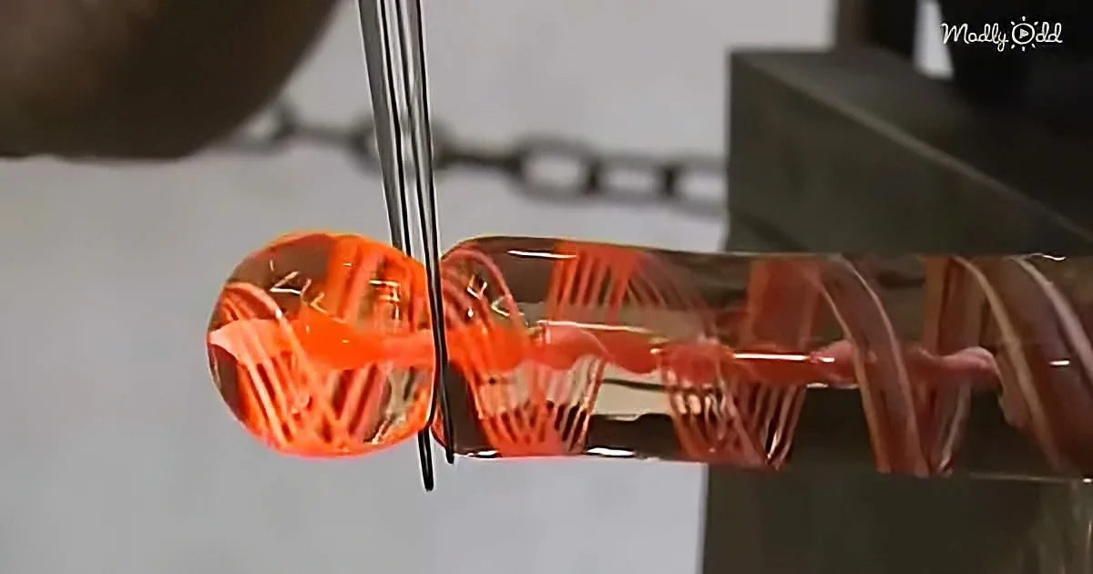 A glassblower uses a tool to shape molten glass into intricate patterns.