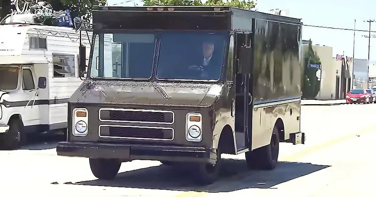 A black delivery truck with a person inside is parked on a street near a white RV.