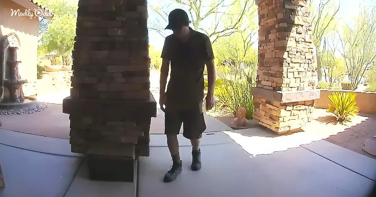 A man in a black shirt and shorts walks on a patio near brick pillars.