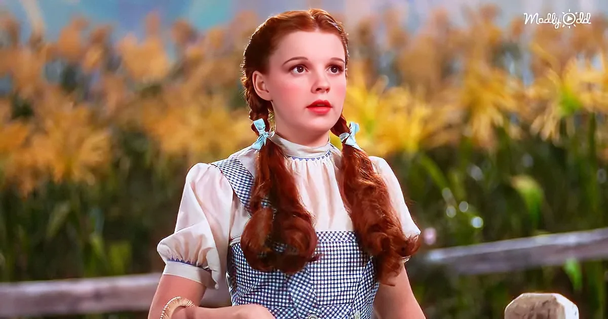 A woman with red braids in a blue and white dress stands in a cornfield, looking off to the side.