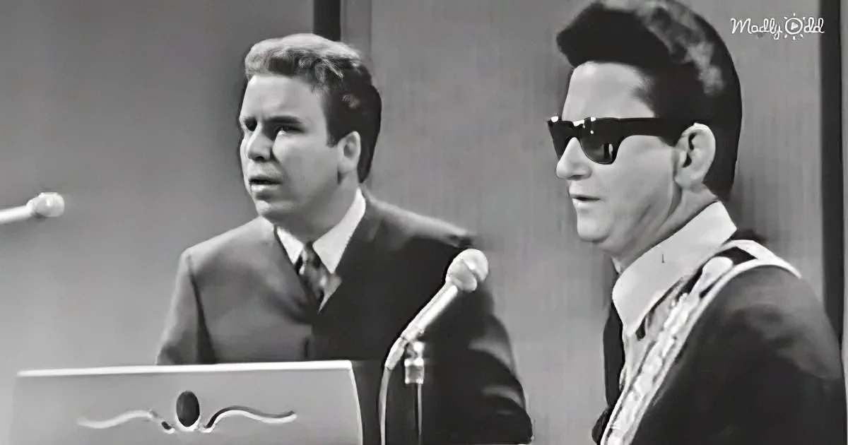 Two men, one in sunglasses, are performing or speaking at a podium with microphones.