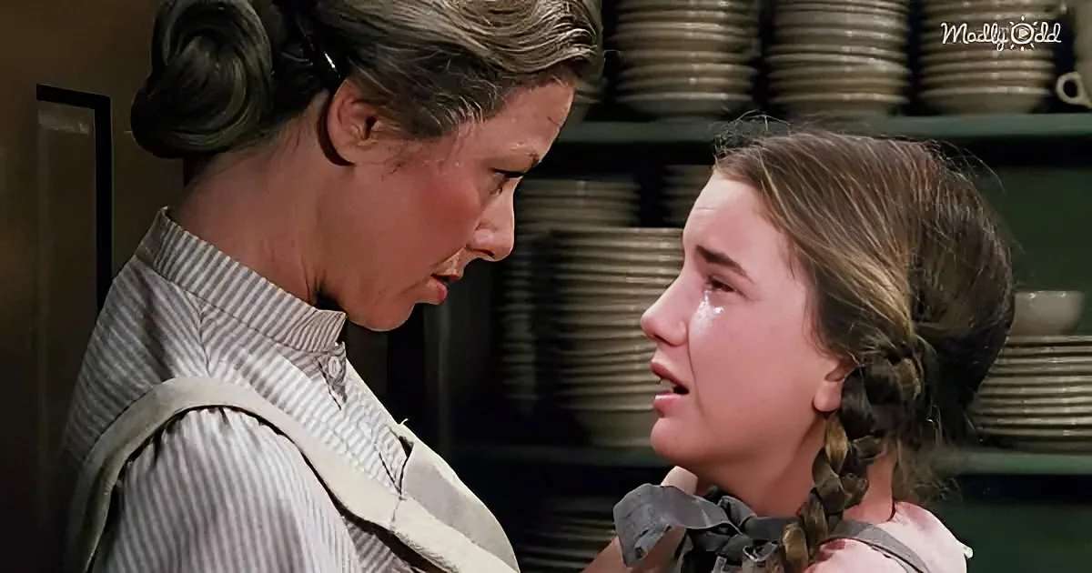 A woman in a striped shirt comforts a crying girl with braids in a kitchen setting.