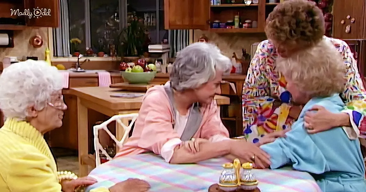 Three elderly women are gathered around a table, engaged in a conversation in a cozy kitchen setting.