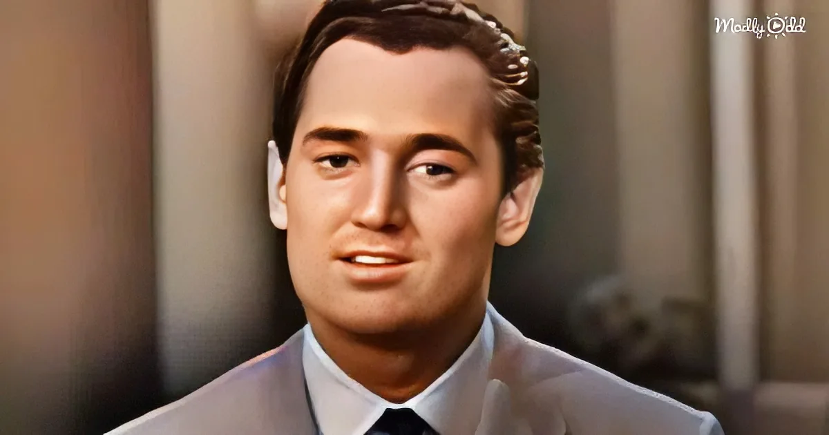 A man in a light suit and tie, looking slightly to the side, with a blurred background.