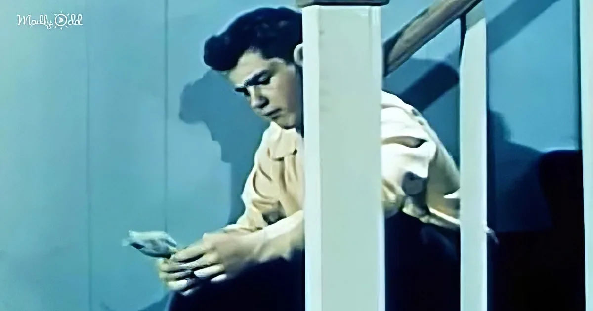 A man in a white shirt leans against a railing, holding a folded piece of paper.