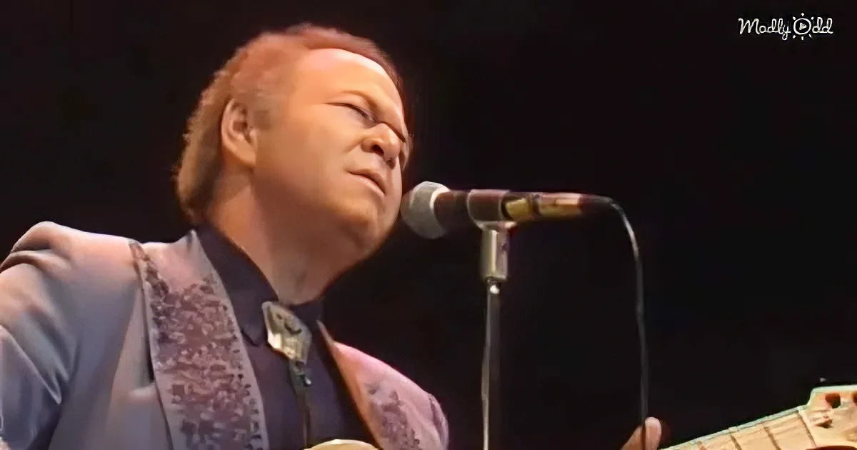A man in a suit plays a guitar and sings into a microphone on stage.