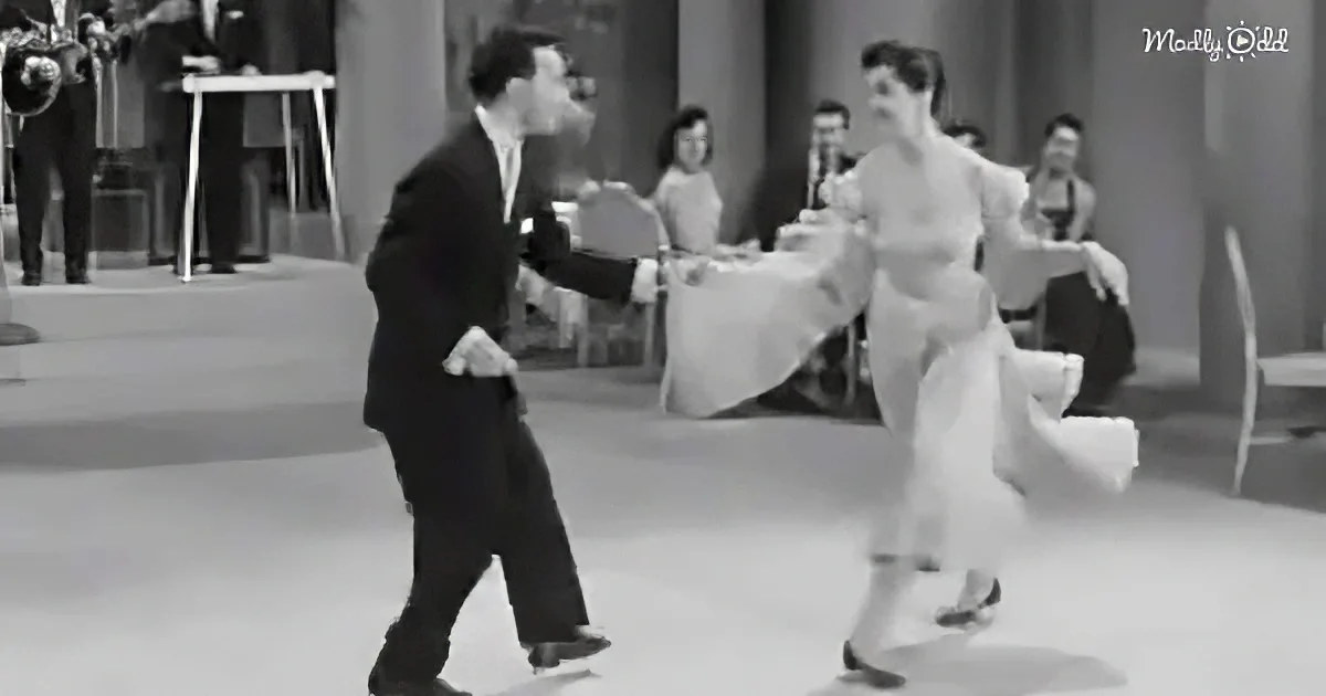 A man and woman are dancing in a black-and-white scene, with the man leading and the woman following gracefully.
