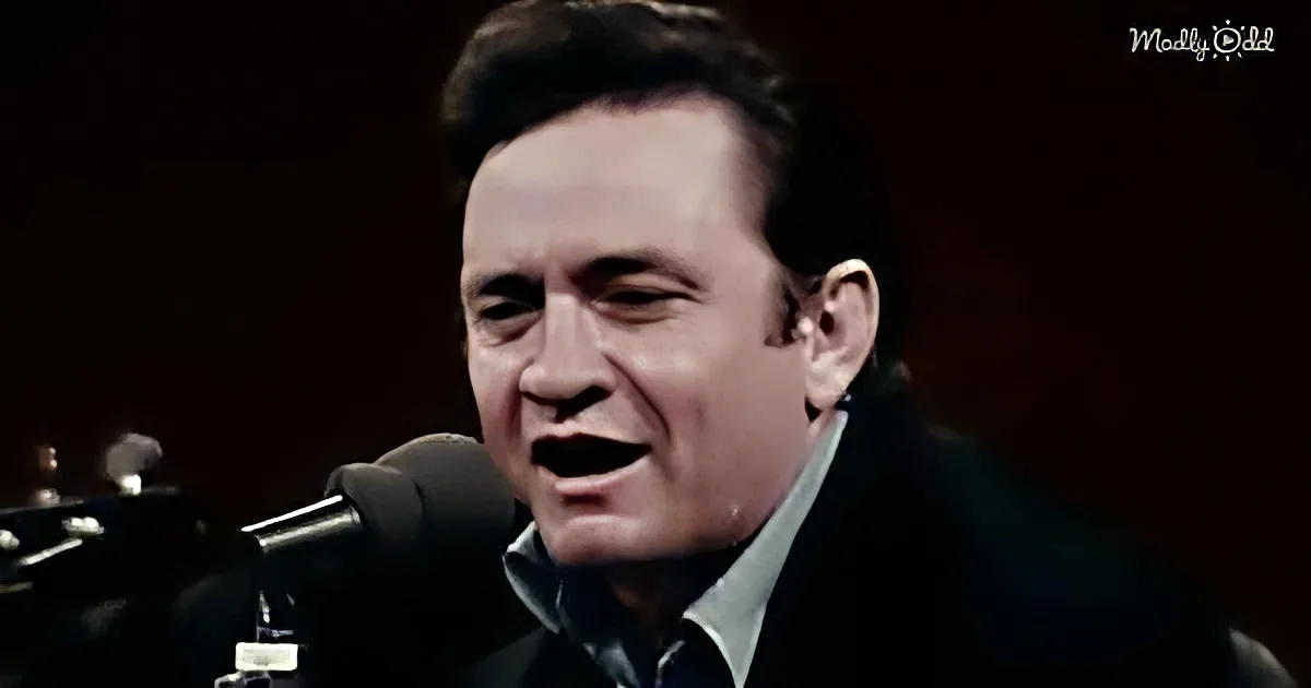 A man in a dark suit sings passionately into a microphone, with a guitar partially visible.