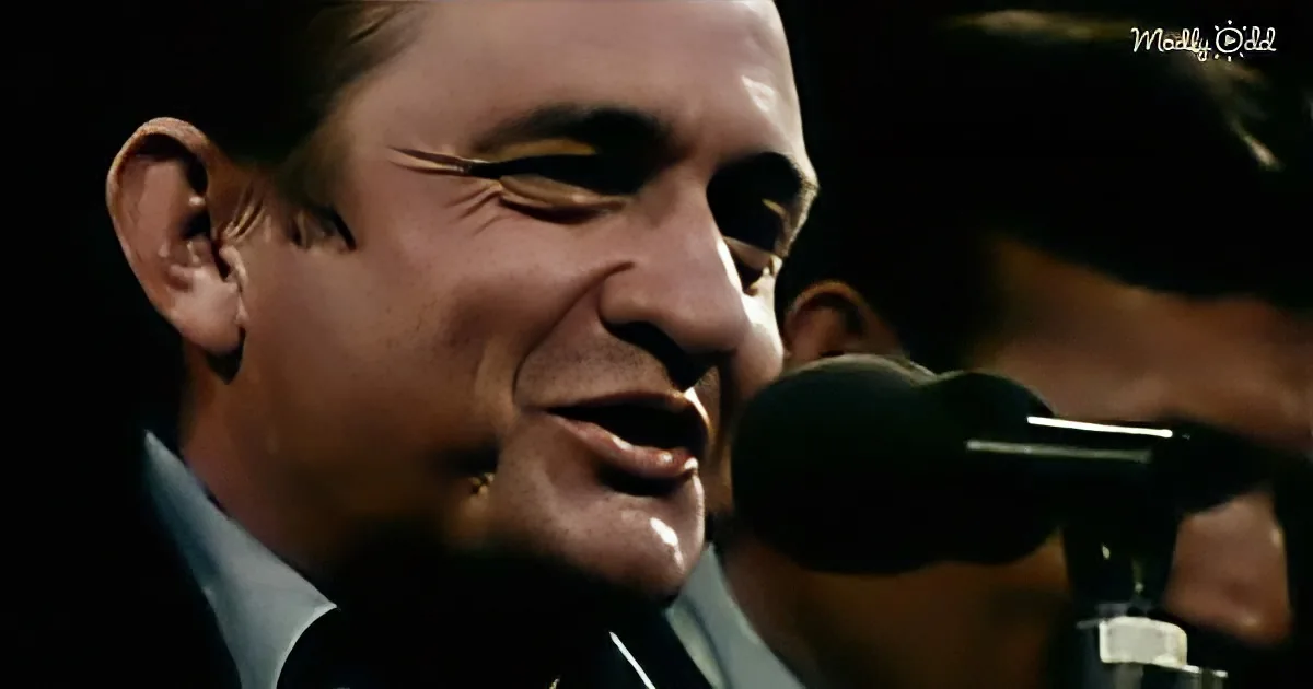 A man in a suit sings into a microphone, his face close to the mic, with another person partially visible behind him.