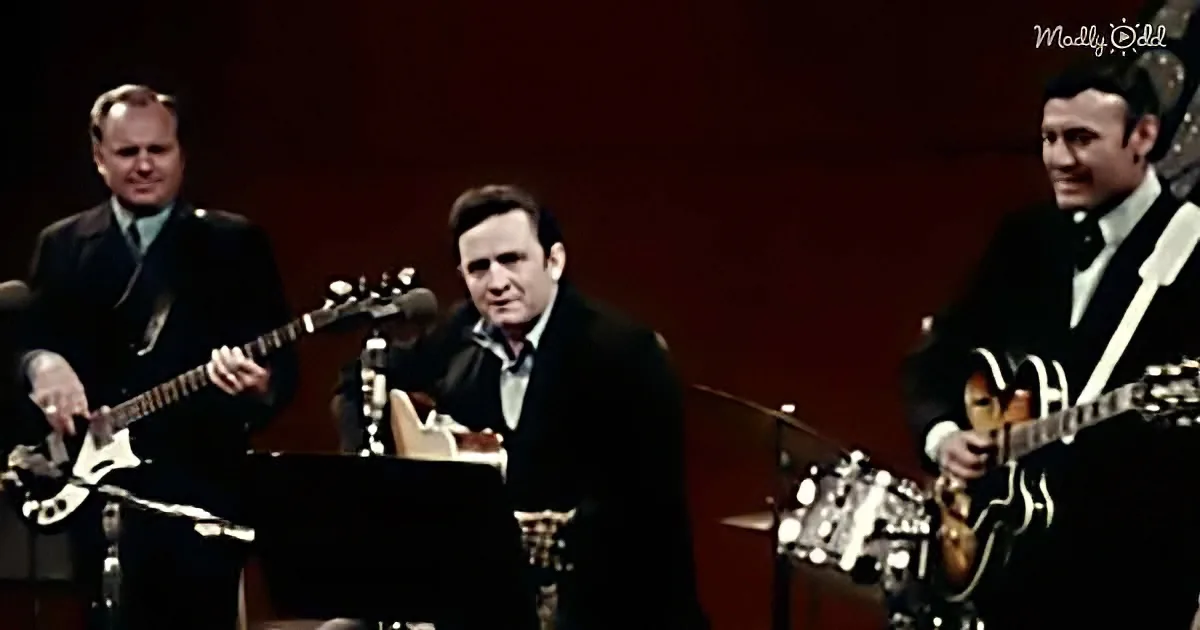 A man in a suit sings on stage with two guitarists, one playing a Les Paul.