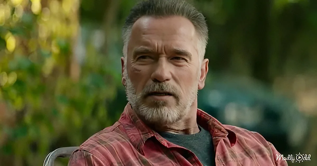 Arnold Schwarzenegger sits outdoors, wearing a red plaid shirt, with a blurred green background.