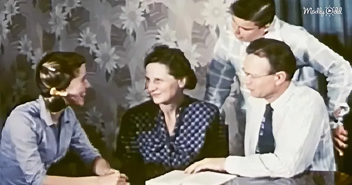 A woman in a polka-dot blouse sits at a table with a man in a white shirt and tie, surrounded by two children.