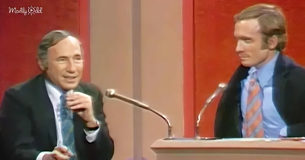 A man in a suit and tie is speaking into a microphone, with another man in a suit and tie standing behind a podium.