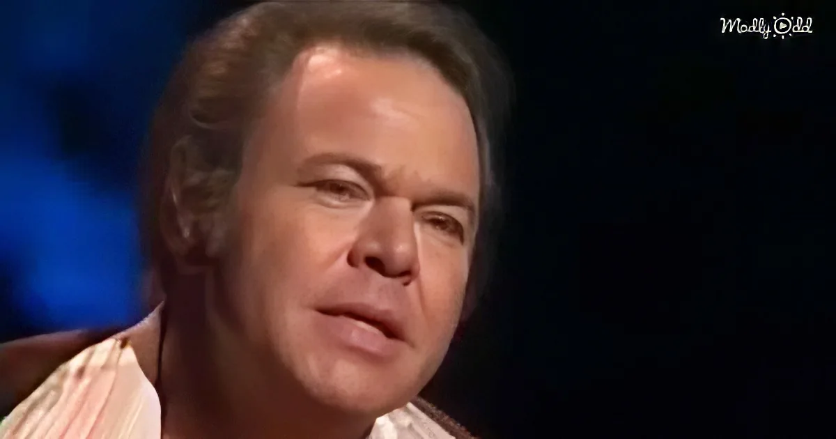 A man with short brown hair, wearing a striped shirt, appears to be speaking or reacting to something.