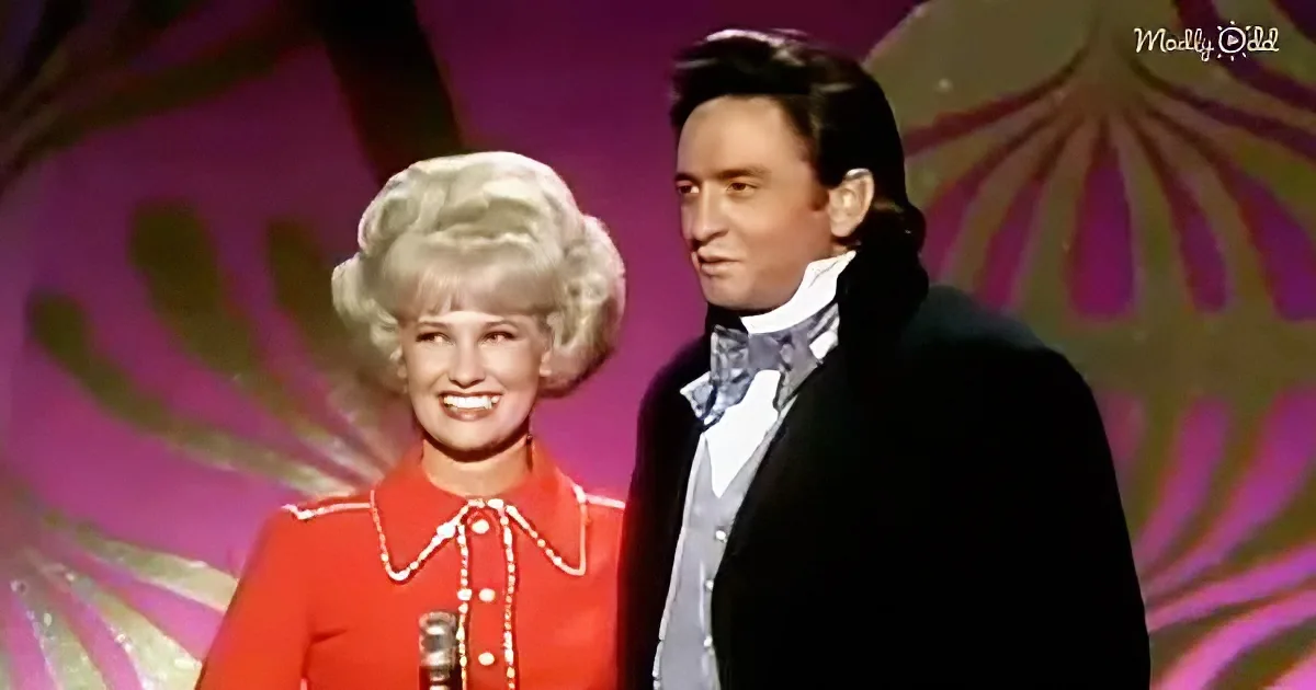 A woman in a red outfit with a pearl necklace and a man in a black suit with a bow tie stand on stage.