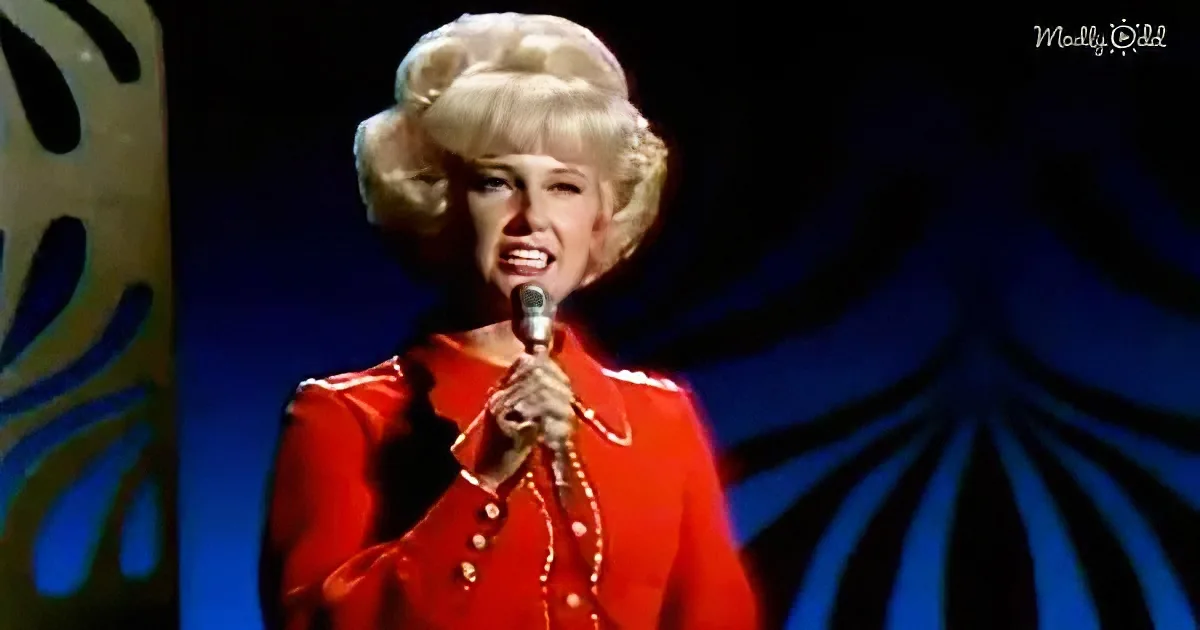 A woman in a red outfit sings into a microphone on stage with a blue and yellow backdrop.