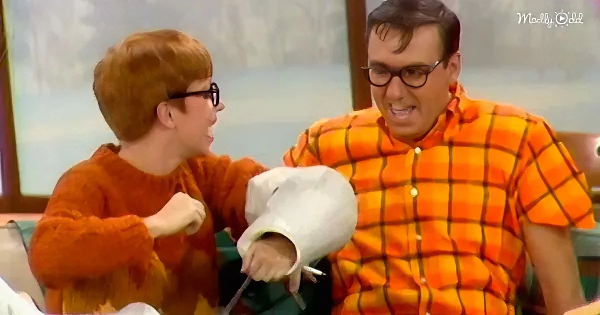 A person in an orange shirt is playfully interacting with another person in a plaid shirt, both wearing glasses.