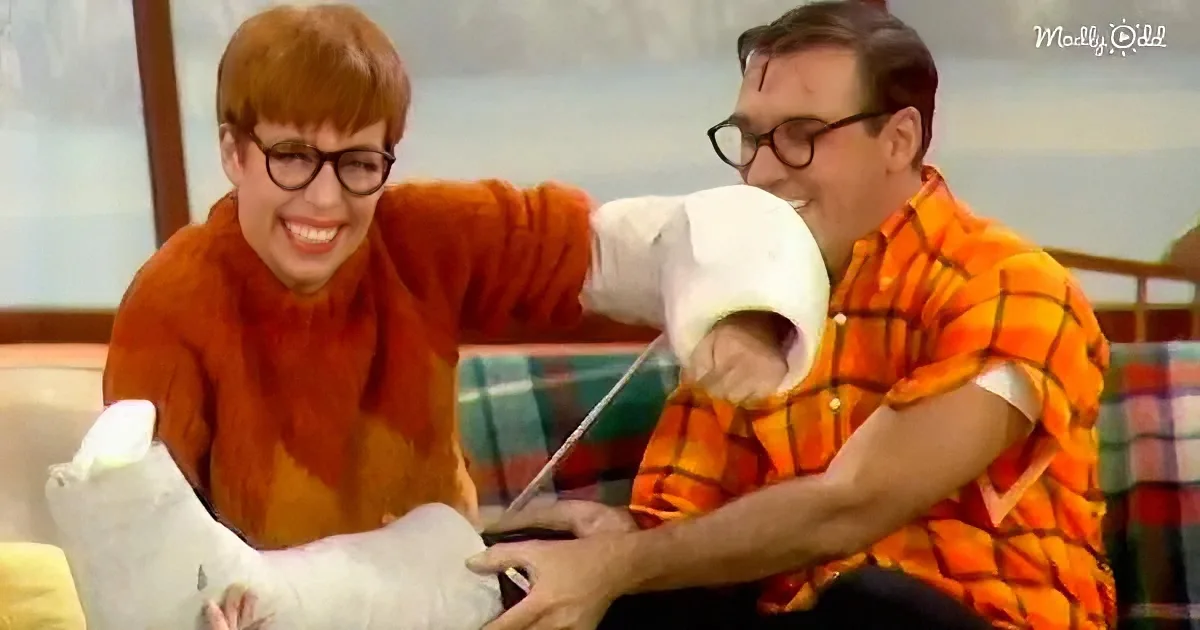 Two individuals in vibrant outfits, one with a cast on their leg, share a moment of laughter and camaraderie.