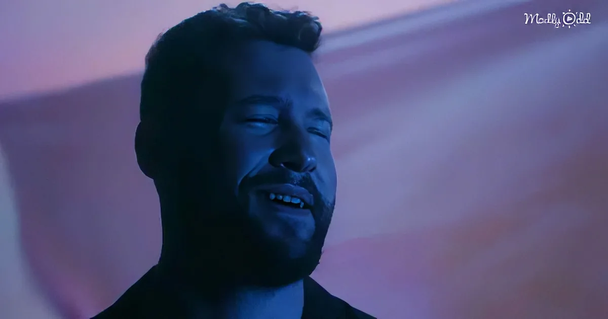 A man with closed eyes and a beard, illuminated by a blue light, appears contemplative or emotional.