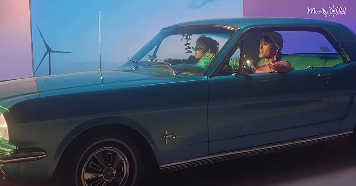 A teal vintage Ford Mustang with two people inside, set against a backdrop of wind turbines and a purple sky.