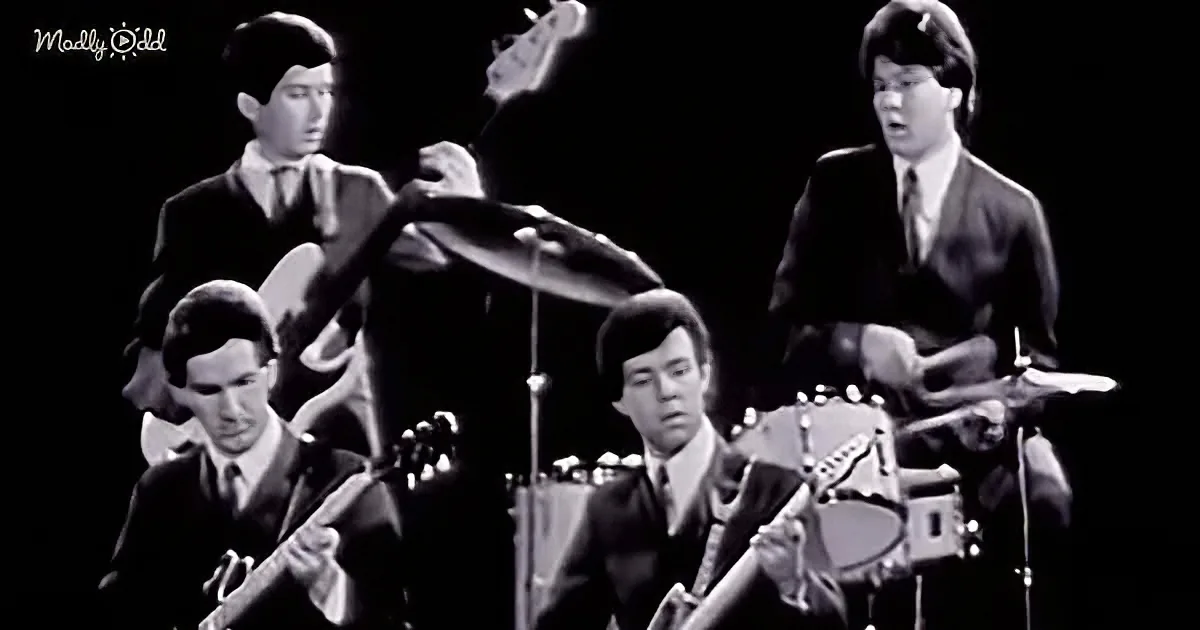 A black-and-white image of a band performing, with musicians playing guitars and drums.