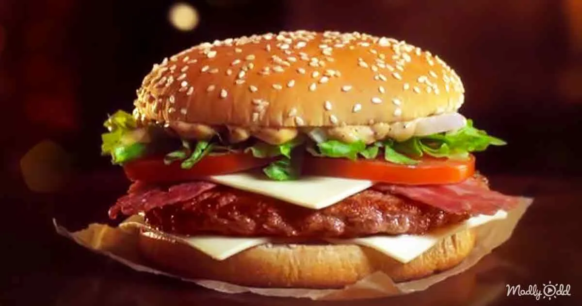A sesame seed bun burger with lettuce, tomato, cheese, bacon, and a beef patty on parchment paper.